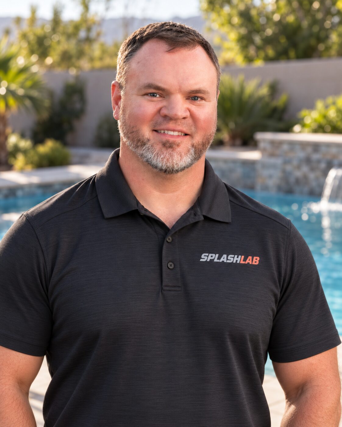 Joseph Livingston of SplashLab Pool Service wearing a SplashLab polo in front of a swimming pool
